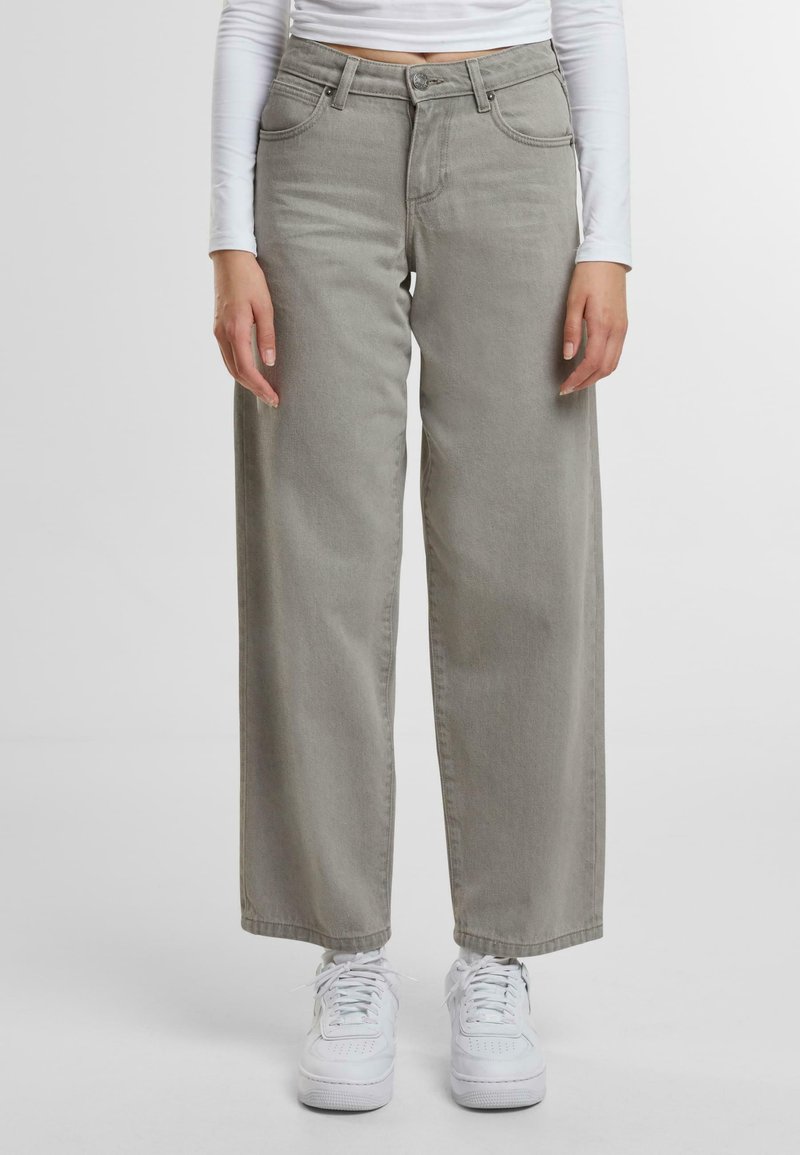 Vaqueros de pierna ancha gris claro con cintura alta, cinco bolsillos y detalles de costura sutiles; combinados con zapatillas blancas.
