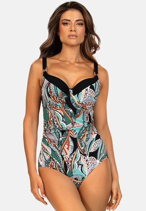 Kobieta w jednoczęściowym stroju kąpielowym z czarnymi ramiączkami i wielokolorowym abstrakcyjnym wzorem, stojąca na tle jednolitego jasnego tła.