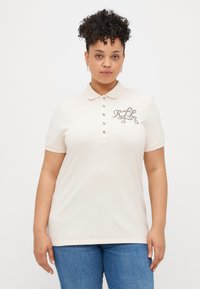 Camisola polo bege com gola e mangas curtas. Apresenta costuras decorativas no peito e na pala dos botões.