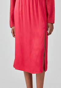 Rosa satengkjole med lange ermer og et sidesnitt. Glatt tekstur med løs passform, elastisk midje for ekstra komfort.