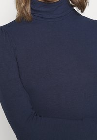 Námořnická modrá roláková svetr vyrobený z žebrované tkaniny, s dlouhými rukávy a přiléhavým střihem, který má měkkou texturu.