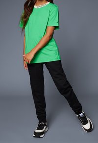 Grön bomullströja med vit rundad halsringning som har "Calvin Klein Jeans"-loggan. Kombinerad med svarta sweatpants och sneakers.