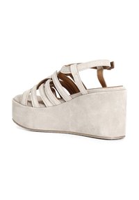 Sandali con zeppa in suede beige con multiple cinghie incrociate e punta arrotondata e liscia. Presentano una piattaforma texture e una cinghia regolabile sul retro.