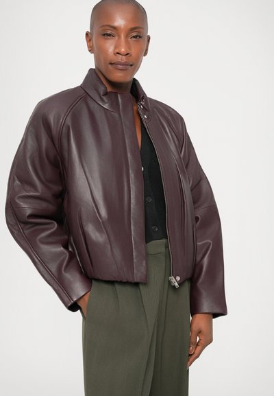 Burgundia nahast bomber-jacket kõrge kaelusega, mugava istuvuse ja tõmblukuga. Kantud musta tipu ja oliivroheliste pükstega.