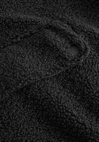 Tissu en polaire noir avec une surface texturée, comportant un petit bouton noir et une couture. Le matériau semble doux et chaud.