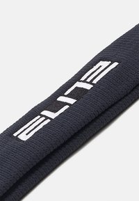 Bandeau en textile noir avec une texture côtelée, comportant un logo brodé blanc et des éléments de design pour le branding.