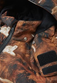 Brun mönstrad jacka med dragkedja, tryckknappar och mjuk svart foder, med en texturerad, abstrakt design över hela.