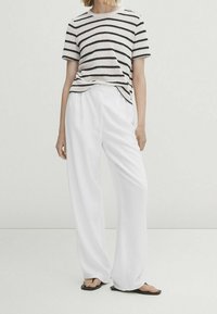 Pasiasta dzianinowa koszulka w kremowo-czarne paski z krótkimi rękawami, zestawiona z białymi szerokimi spodniami. Strój ma luźny krój.