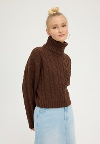 Brown cable-knit turtleneck sweater with ribbed hem and cuffs, paired with a light blue denim skirt. Smooth texture and relaxed fit.