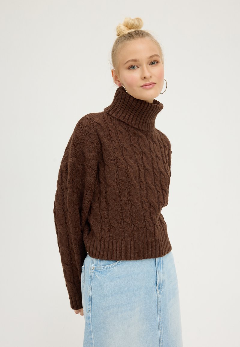 Brown cable-knit turtleneck sweater with ribbed hem and cuffs, paired with a light blue denim skirt. Smooth texture and relaxed fit.