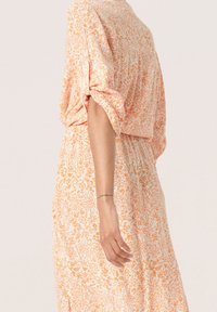 Šaty s květinovým vzorem v oranžové a bílé barvě; měkká, lehká látka; volný střih s krátkými rukávy a elastickým pasem.