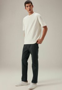 Weißes T-Shirt mit kurzen Ärmeln, kombiniert mit dunklen Hosen und weißen Turnschuhen. Einfacher, lässiger Schnitt mit Rundhalsausschnitt und glatter Textur.