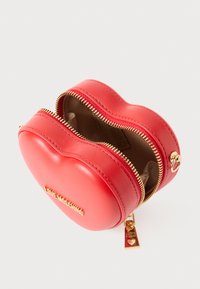 Borsa in pelle a forma di cuore rosso con una trama liscia, zip dorata e un attacco per charm. Interno foderato in tessuto beige.