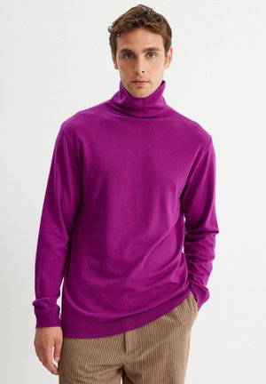 Jersey de cuello alto morado hecho de tejido suave, con mangas largas y un diseño ajustado. Combinado con pantalones de pana beige.