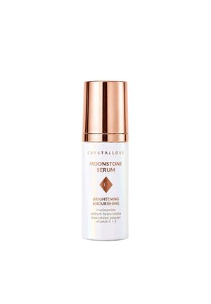 Biała butelka z różowo-złotą zakrętką oznaczona jako Moonstone Serum, rozjaśniająca i odżywcza z niacynamidem, kwasem hialuronowym sodu, proszkiem z kamienia księżycowego, witaminami C i E.