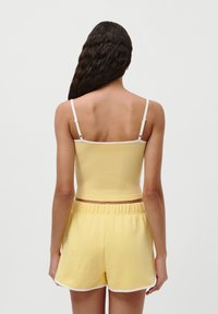 Gul ribbet crop topp med hvite stropper, kombinert med gule shorts med elastisk midje som har hvite kanter. Sett fra baksiden.