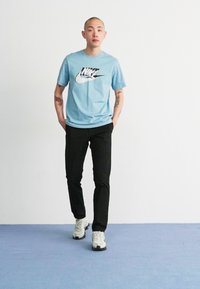 Light blue Nike t-shirt with black logo, paired with black pants and white sneakers. The outfit features a simple, casual design.