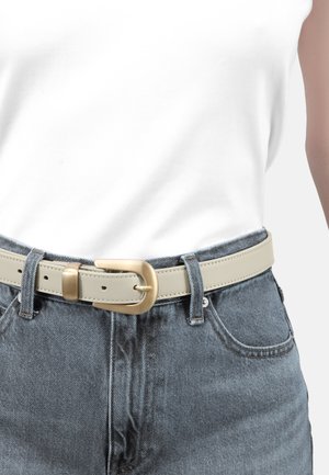 Hellebeige Leder-Gürtel mit einer goldenen ovalen Schnalle, getragen über hochtaillierten blauen Jeans und einem schlichten weißen Oberteil.