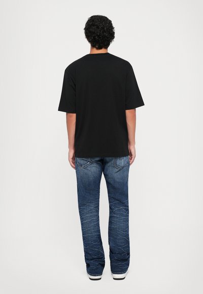Mustmust särk lühikeste varrukatega, millel on ülekaaluline lõige, koos helesiniste denim teksadega, millel on nähtavad õmblused ja kergelt kulunud tekstuur.