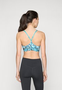 Sportinė liemenėlė su mėlynu abstrakčiu raštu, reguliuojamomis žalsvomis petnešomis ir lygiu paviršiumi. Pora su aukštai juosmeniu tamsiomis leggins. 