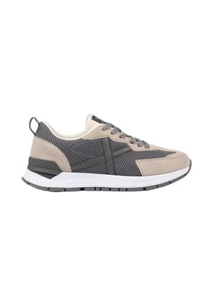 Zapatilla informal en malla beige y gris oscuro con superposiciones de ante, suela blanca, cordones grises y cinta en el talón, mostrada de perfil.