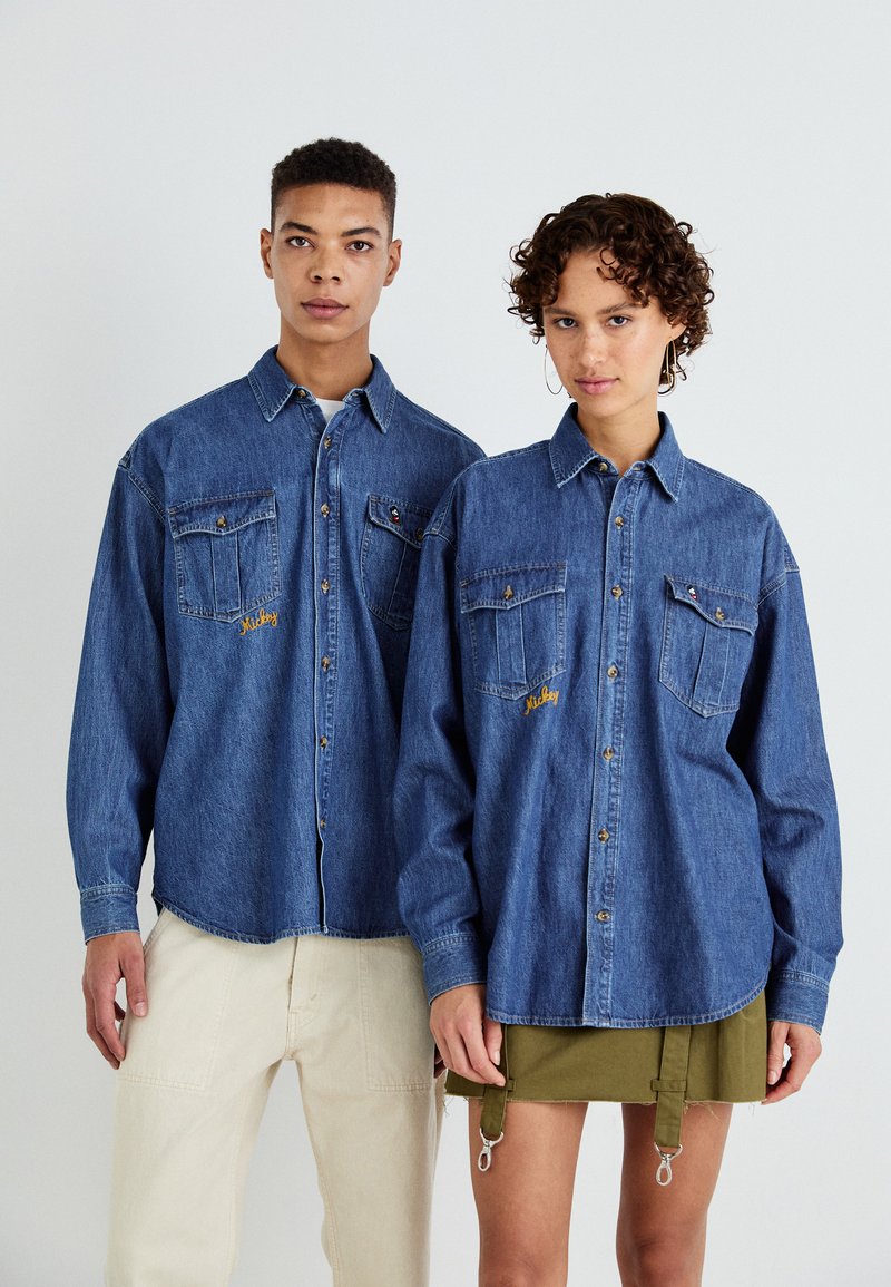 Denimskjorter for voksne, med lange ermer, to brystlommer og gult broderi, kombinert med lyse beige og olivengrønne bukser.