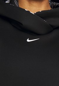 Sweat à capuche noir Nike avec logo swoosh blanc sur la poitrine, porté par une personne montrant le cou et une partie de la mâchoire en gros plan.