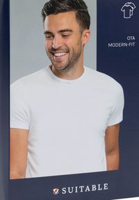 Weißes modern geschnittenes T-Shirt mit kurzen Ärmeln, rundem Halsausschnitt und glattem Baumwollstoff. Auf einem blauen Hintergrund mit Verpackungsdetails präsentiert.