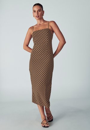Brown patterned midi dress with thin straps, fitted silhouette, and a geometric design. Paired with black strappy sandals.