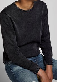 Chemise longue à manches longues en coton gris foncé, avec un col rond, un tissu texturé et des accents de couture contrastants au niveau du col et des poignets.