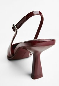 Pantof cu toc mediu, din piele lucioasă de culoare burgundy, cu vârf pătrat și curea ajustabilă cu cataramă argintie.