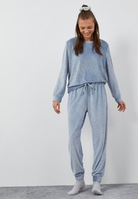 Jasnoniebieski zestaw odzieży domowej składający się z luźnej bluzy z długim rękawem o prążkowanej fakturze oraz pasujących spodni dresowych z wiązaniem w talii i ściągaczami.