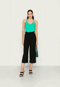 Top de alças finas em turquesa, combinado com culottes pretas de cintura alta. Acessórios incluem uma bolsa verde e sapatos de salto pretos.