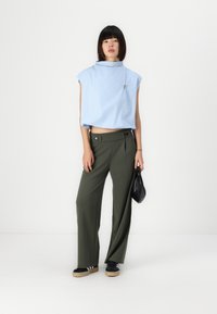 Top corto azzurro chiaro con maniche corte e colletto, abbinato a pantaloni a gamba larga color verde oliva a vita alta. Borsa e scarpe nere.