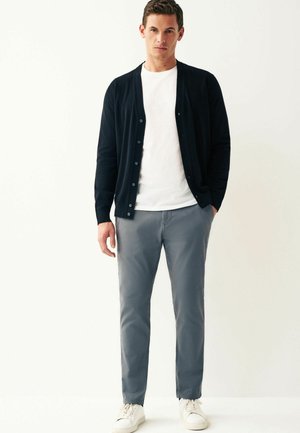 Cardigan navy, maglia leggera con bottoni, sopra una t-shirt bianca. Pantaloni grigi aderenti e sneakers bianche completano l'outfit.