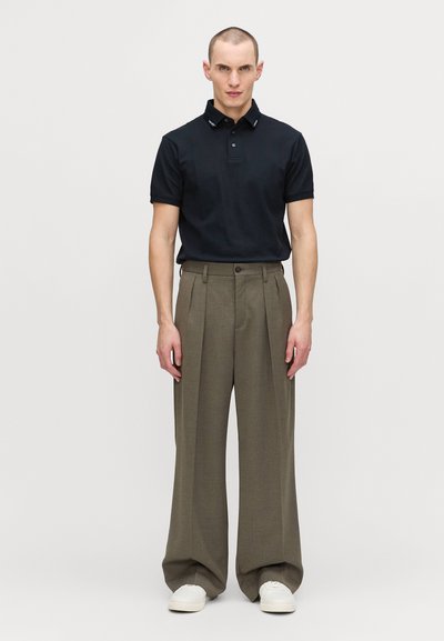 Marinblå pikétröja med krage, kombinerad med högmidjade, vida olivgröna byxor och vita sneakers. Minimalistisk design och neutrala färger.