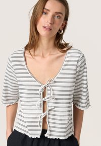 Csíkos crop top fehér és fekete színben, mély V-nyakkal, megkötőkkel, rövid ujjal és fodros szegéllyel. Texturált anyagból készült.