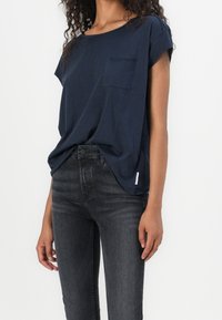 Námořnická modrá tričko s krátkým rukávem a kulatým výstřihem, s kapsou na prsou, vyrobené z měkké tkaniny. V kombinaci s tmavě šedými skinny džíny.