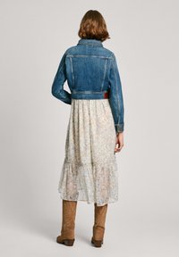 Chaqueta de mezclilla con un estilo ajustado, color azul y costuras sutiles. Vestido con patrón floral en capas, con un dobladillo con volantes y colores suaves.