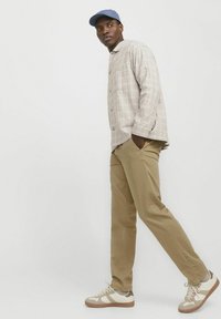 Light plaid button-up shirt with long sleeves, beige trousers, and beige sneakers with white accents and textured sole. Blue cap completes the look.