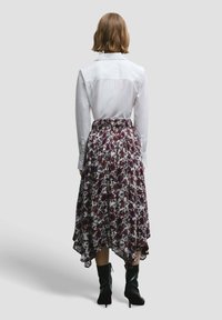 Witte blouse met lange mouwen, gecombineerd met een knielange rok met bloemenpatroon in paarse en witte tinten, gedragen met zwarte enkellaarsjes.