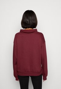 Sudadera sobre tamaño en color marrón con un cuello de tortuga, hombros caídos y dobladillo acanalado. Textura suave con mangas largas y un corte holgado.