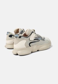 Beige textured sneakers with black and light blue accents, featuring a chunky sole and layered design. Branding displayed on the heel.