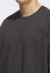 Dark gray cotton t-shirt with a crew neck, featuring a subtle black three stripes logo on the left side of the chest. Smooth texture.