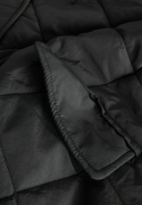 Giacca nera imbottita con un design trapuntato, caratterizzata da una texture liscia e un colletto ripiegato. Cuciture decorative visibili lungo i bordi.