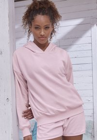 Felpa rosa chiaro con una vestibilità rilassata e profondo scollo a V, abbinata a pantaloni corti coordinati. Realizzata in tessuto morbido con polsini e orlo a coste.