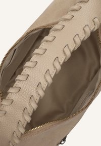 Beige handtas met gevlochten leren handvat, open gouden rits en een gladde beige stoffen binnenvoering zichtbaar.