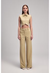 Beige gekapte mouwloze top met een kraag en een diagonale zoom, gecombineerd met hoog gewaagde, wijde pantalons in bijpassende stof. Soepele textuur.
