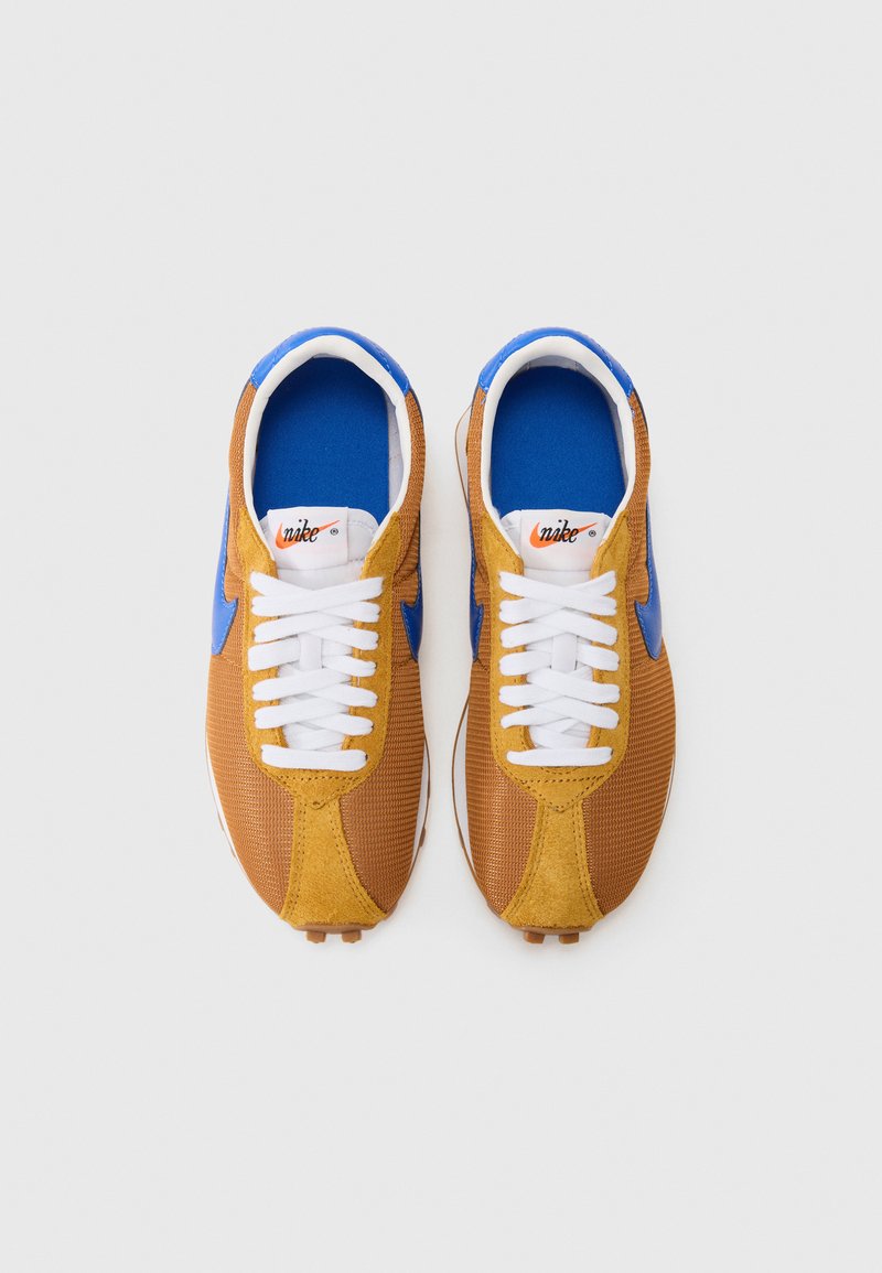 Sneakers Nike w odcieniach brązu i niebieskiego, wykonane z materiału siateczkowego i zamszowego, z białymi sznurowadłami, wyściółką w kolorze niebieskim oraz charakterystycznym logo Swoosh.