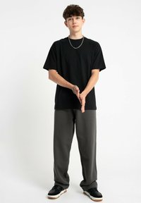 Czarna koszulka z krótkim rękawem, luźny krój, w zestawie z szerokimi szarymi spodniami. Czarne sneakersy z białymi podeszwami. Prosty dodatek: srebrny łańcuszek. 